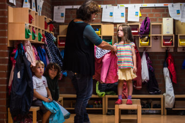 Eine Erzieherin hilft einem Mädchen beim Anziehen der Jacke.