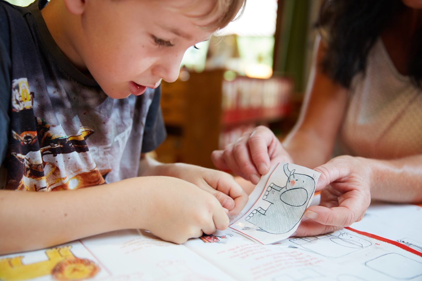 Ein Junge klebt einen zuvor aus einem Bilderbuch geschnittenen Elefanten wieder in das Buch.
