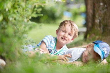 Zwei Jungen liegen auf dem Kita-Gelände im Gras.