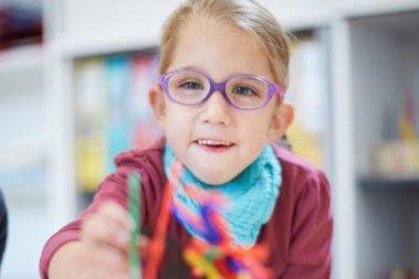 Lia sitzt an einem Tisch im Spielraum der Kita Pusteblume in Windesheim und malt. Sie ist mit einem Genfehler geboren und hat einen höheren medizinischen Unterstützungsbedarf.