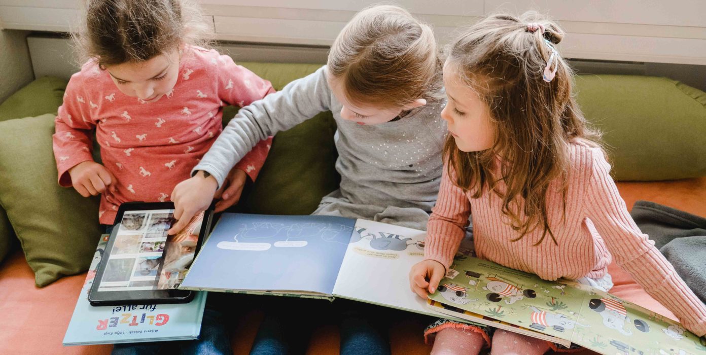Kinder schauen sich Bücher an und recherchieren in einem Tablet