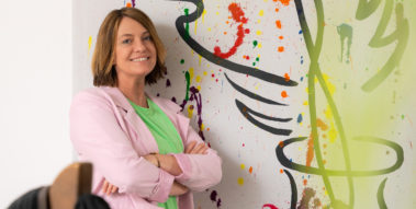 Frau lehnt an bunt bemalter Wand.