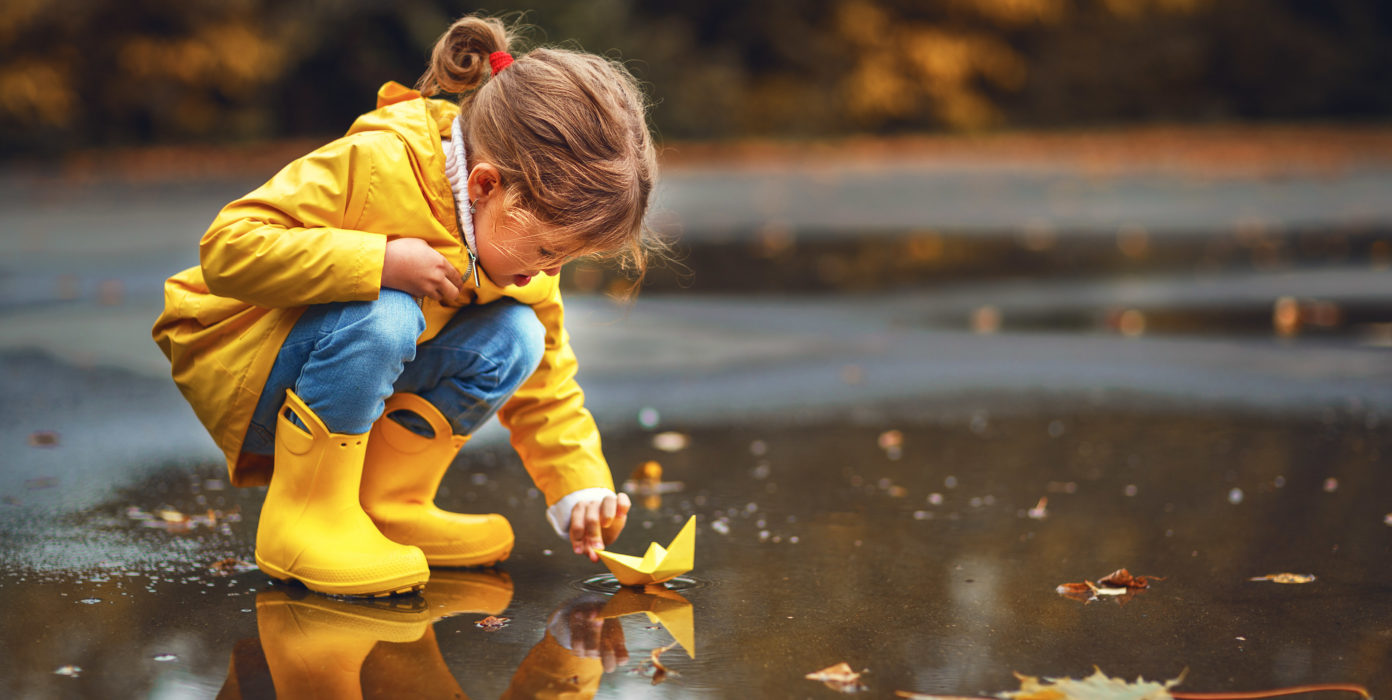 Kind spielt in Pfütze mit einem Papierschiff