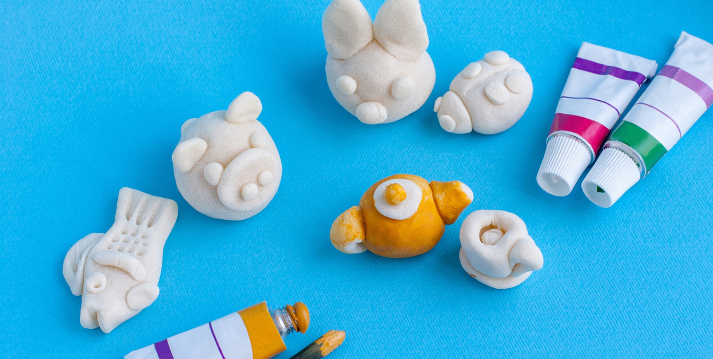 Auf einer blauen Untelage leigen mehrer aus Salzteig beformte Figuten wie ein Fisch oder ein Schweinchen. Einige sind bereits bemalt.