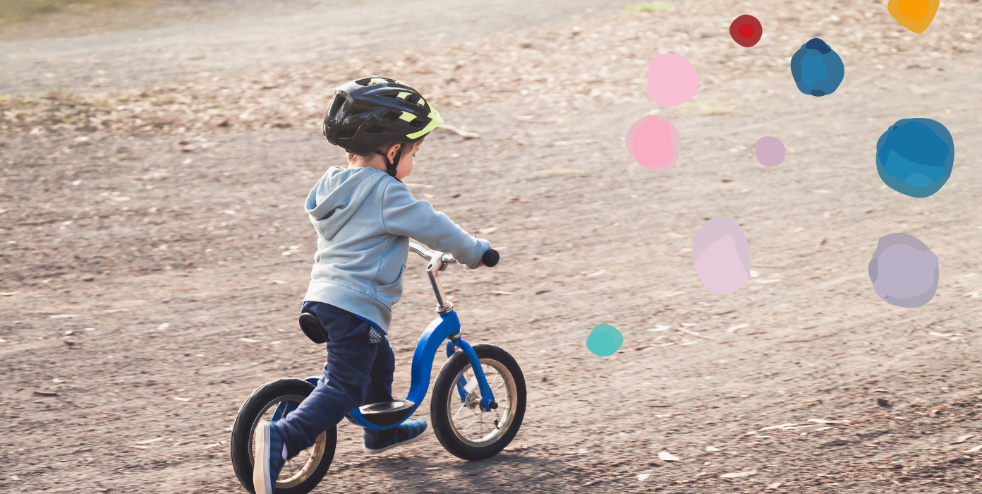 Kleiner Junge mit Helm fährt Laufrad.