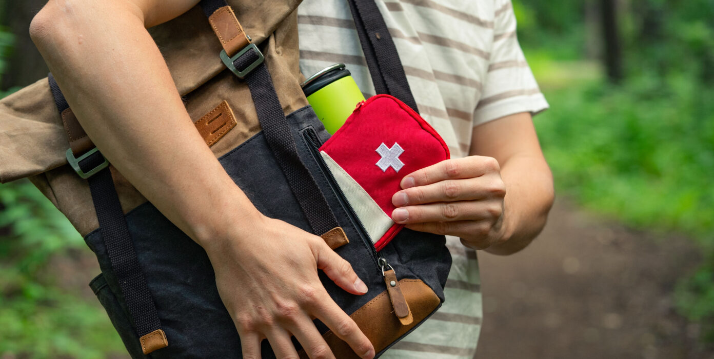 Ein Rucksack, aus dem jemand eine kleine Erste-Hilfe-Tasche herausholt.