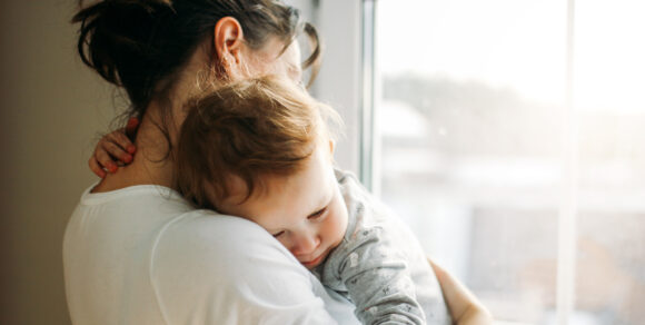 Ein Kind auf dem Arm einer Frau kuschelt sich an sie.