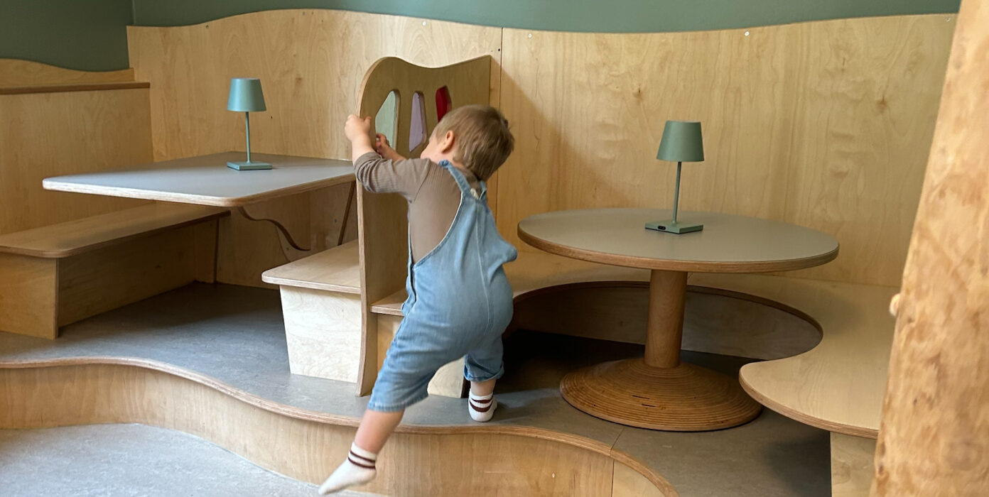 Kleinkind klettert eine Stufe zu einer Sitzecke mit einem tisch hoch.