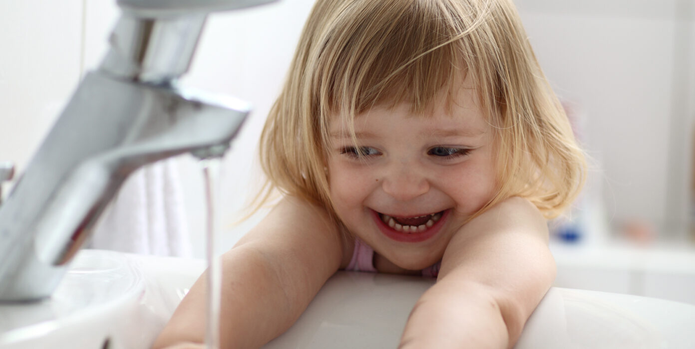 Ein Kind spielt an einem Waschbecken mit Wasser.