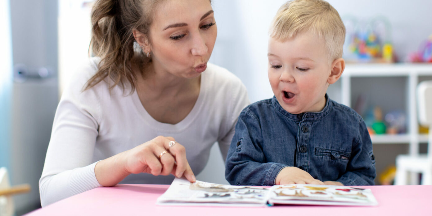 Eine Erzieherin spricht mit einem Kind über ein Kinderbuch.
