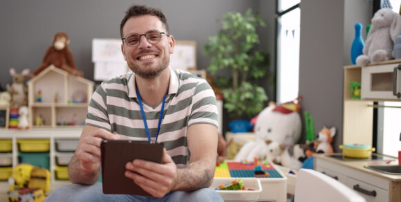 Ein Mann sitzt mit einem Tablet in einer Kita.
